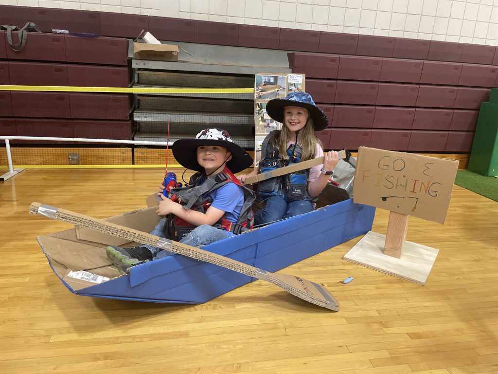 two boys in a cardboard boat with paddles