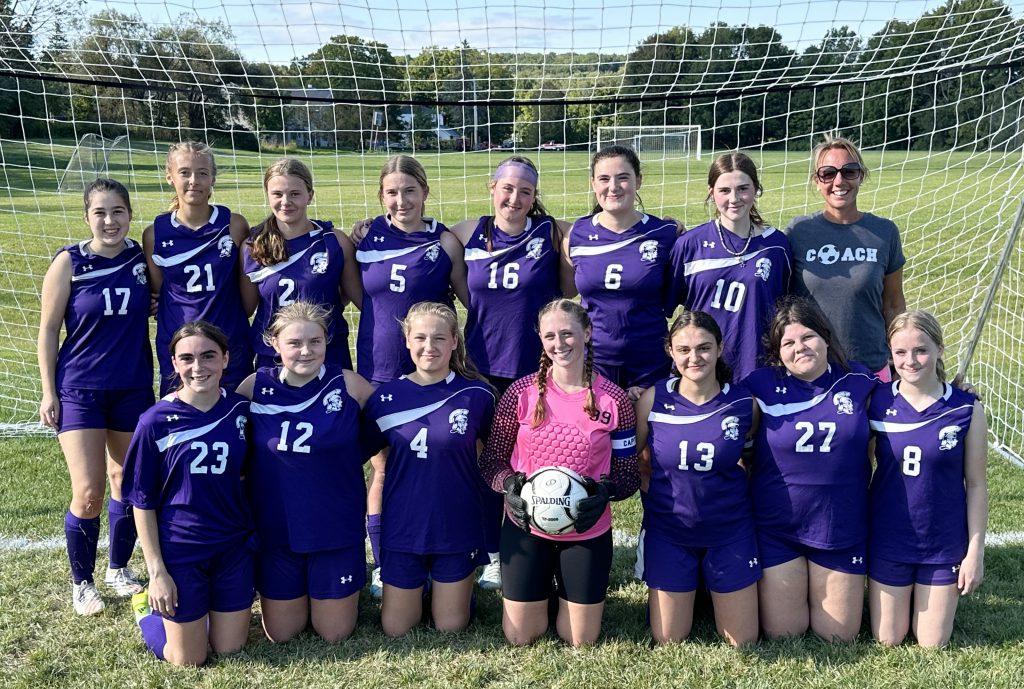 group of girls pose in front of soccer goal wearing their purple uniforms