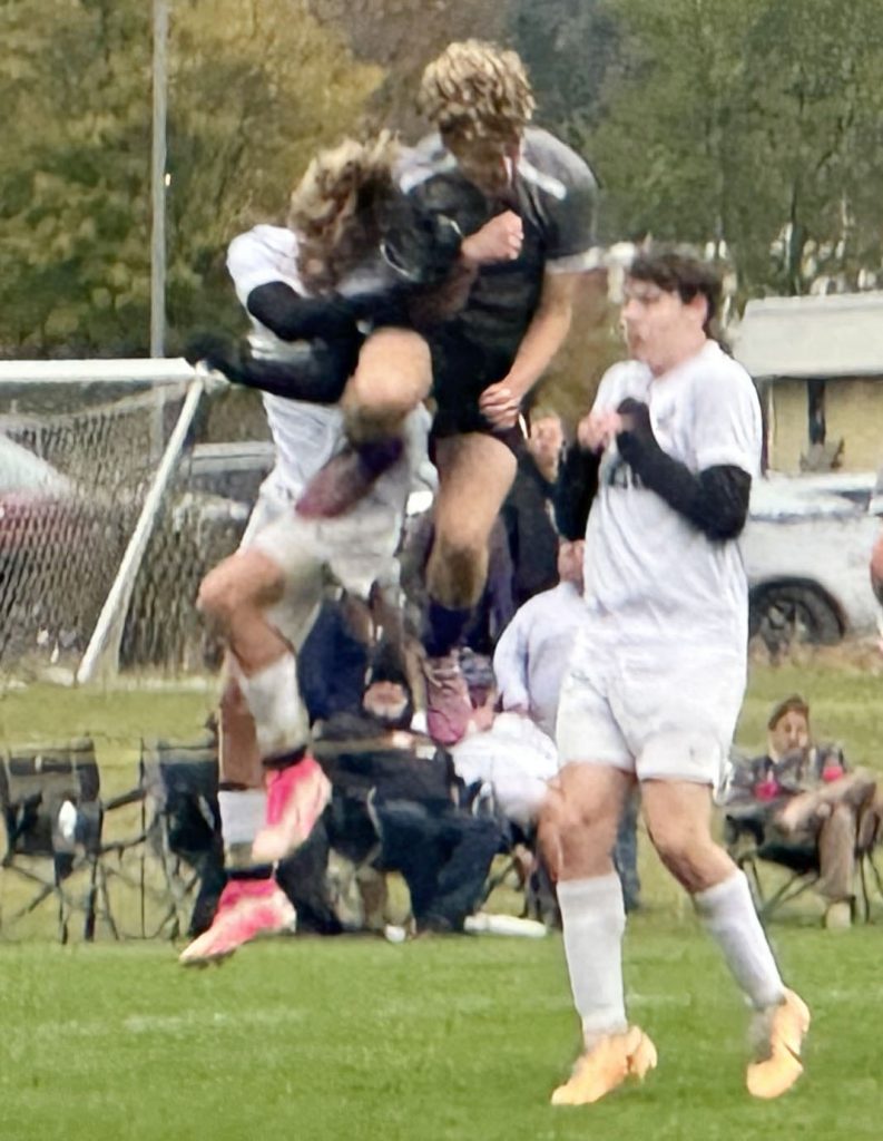 boy jumps for soccer ball depended by two other players