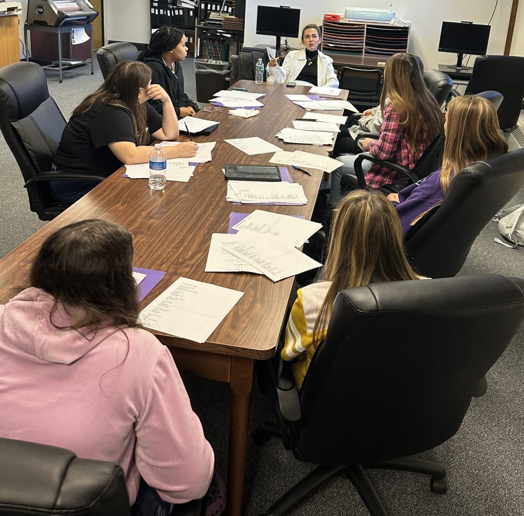 students work at a conference table with a female poet