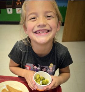 girl holding cup of veggies and smiling