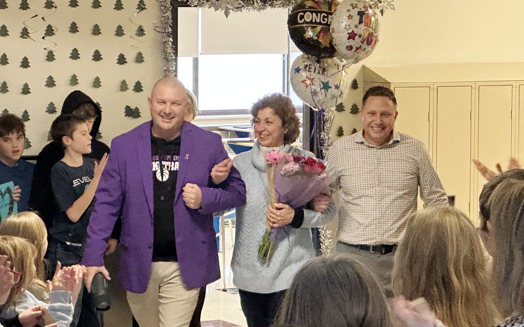 two men escort woman carrying flowers on walk out of school as strudents salute her parade style