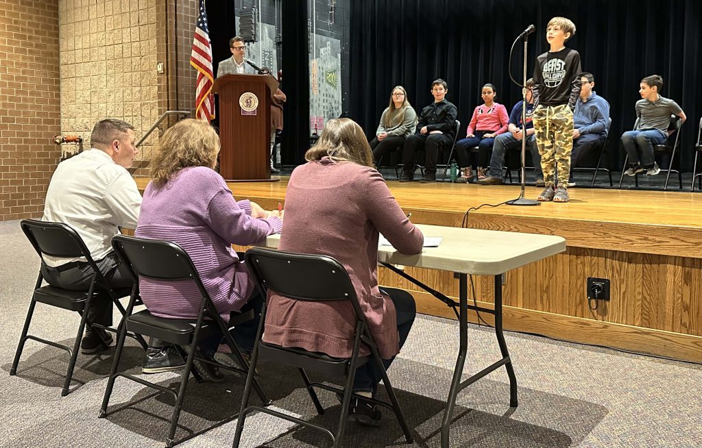 student spells a word on stage in front of three judges